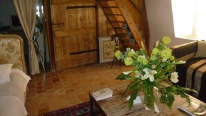 Quarto rústico com vigas de madeira, porta de madeira, escada, sofá e mesa com um vaso de flores.