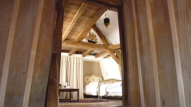 Escada de madeira que leva a um quarto com uma cama e um candeeiro suspenso.