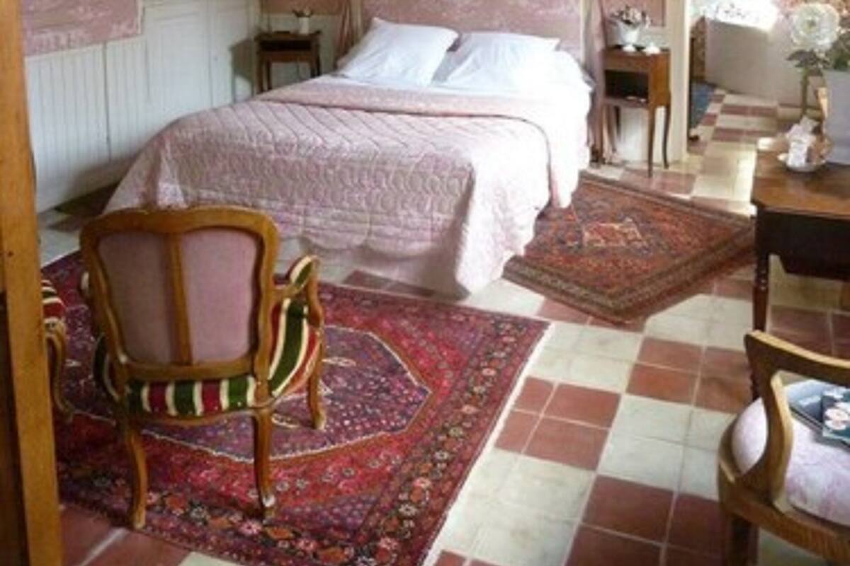 A bedroom with a large bed, a canopy, a wooden chair, a small table, and a patterned rug.