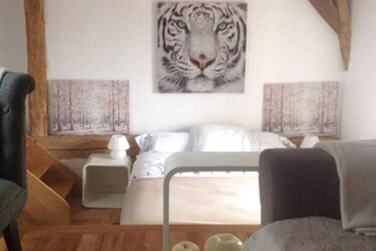 A bedroom with a large tiger painting on the wall, a bed with white bedding, a nightstand, and a small table with apples.