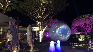 A nighttime outdoor area with illuminated trees, a large spherical light installation, and a building with signage. - Villa Flores, Vale do Lobo - modern 4 bed, 4 bath, south facing villa with pool  (Almancil)
