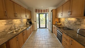 A kitchen with wooden cabinets, granite countertops, a tiled backsplash, and a herringbone-patterned floor. - Villa Flores, Vale do Lobo - modern 4 bed, 4 bath, south facing villa with pool  (Almancil)