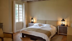 Une chambre à coucher avec un grand lit, deux tables de chevet avec des lanternes, une chaise et une fenêtre avec des rideaux.