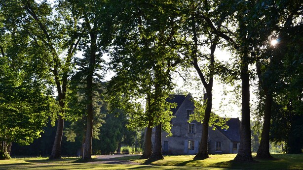 Un bâtiment en pierre doté d’un toit en pente, entouré d’une zone herbeuse parsemée d’arbres.