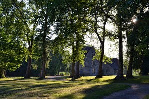 Un bâtiment en pierre doté d’un toit en pente, entouré d’une zone herbeuse parsemée d’arbres.