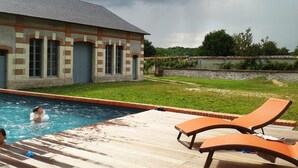 Une piscine avec des chaises longues, un bâtiment à la façade en briques et une zone herbeuse.