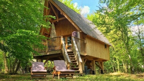 A wooden cabin with a staircase leading to a deck, surrounded by trees.