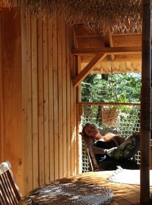 A wooden cabin with a thatched roof, a hammock, and a woven mat on the floor. - Ecolodge Beauregard (Treigny-Perreuse-Sainte-Colombe)