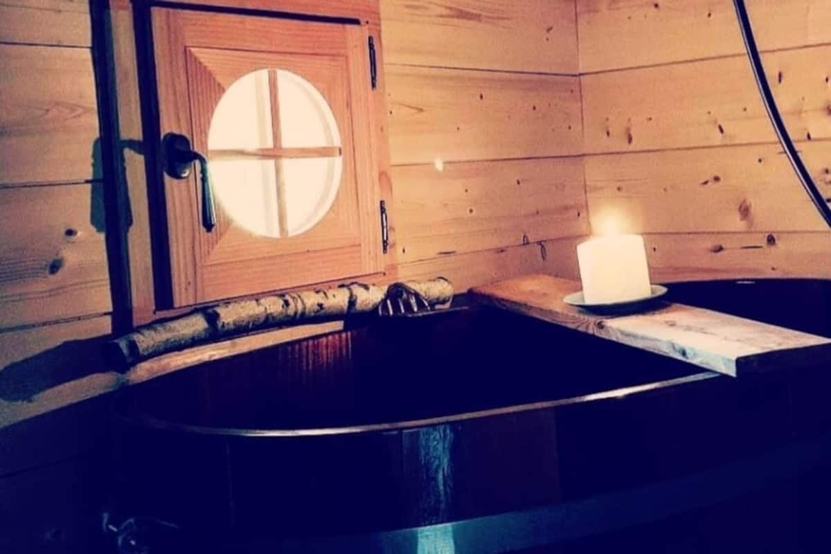A wooden cabin interior with a wooden door, a candle on a table, and a window with a circular design.