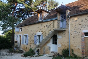 A two-story stone house with a balcony, a staircase, and a small garden area with outdoor furniture. - Ecolodge Beauregard (Treigny-Perreuse-Sainte-Colombe)