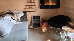 A cozy room with a sofa, a black chair, a glass table with candles, and a menu board.