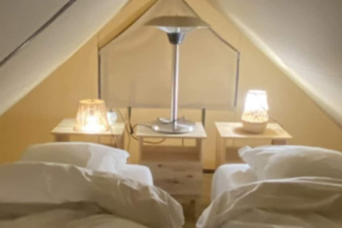 A small, cozy attic bedroom with two beds, a central table, and two bedside lamps.