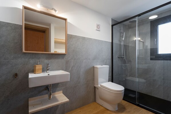 Un baño moderno con un lavabo blanco, un inodoro y una ducha con mampara de vidrio.