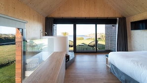 Une chambre moderne avec un plafond en bois, un balcon doté de rampes en verre, un lit et une vue sur l’extérieur.
