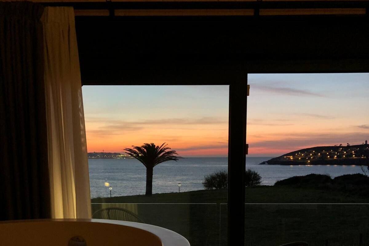 A balcony with a view of a sunset over the sea, a palm tree, and a distant town.