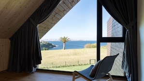 Une pièce dotée d’une grande fenêtre donnant sur la côte, d’un fauteuil et de murs en bois.