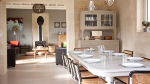 Een eethoek met een lange tafel gedekt voor vier personen, omringd door rieten stoelen. Achterin is een wit kastje met glazen deuren te zien.