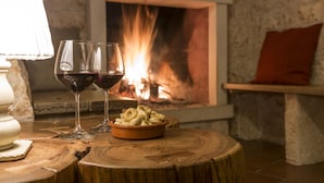 Une pièce chaleureuse avec une cheminée, deux verres à vin et un bol de collations sur une table en bois.