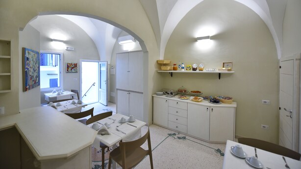 Un comedor con mesa dispuesta para dos, una cocina con barra desayunadora y un pasillo que conduce a otra habitación.