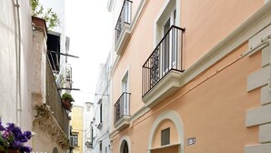 Una calle estrecha flanqueada por edificios, con balcones de barandilla metálica y una tapa de alcantarilla en el suelo.