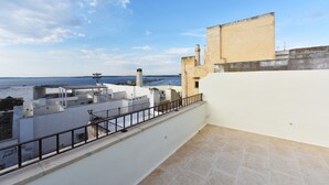 Una terraza en la azotea con vista al mar, con una pared blanca y un edificio color beige al fondo.