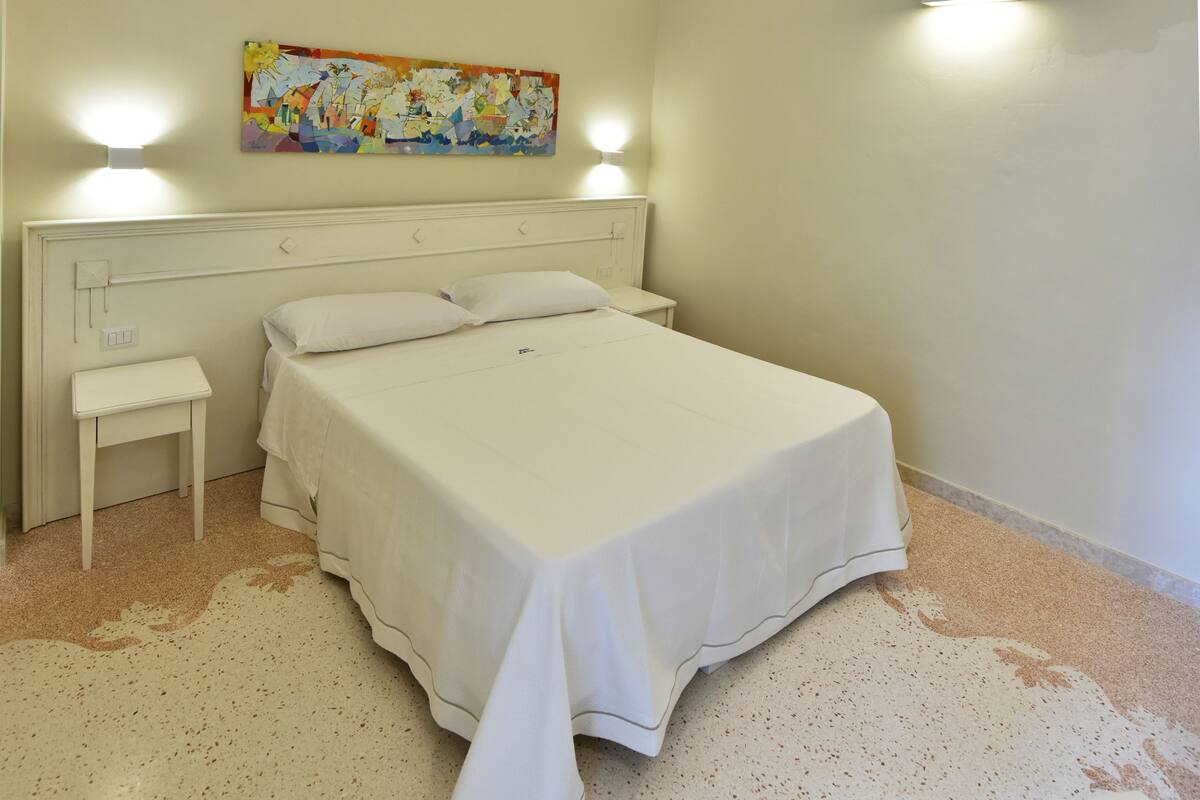 Een slaapkamer met een bed, nachtkastje en een schilderij aan de muur.