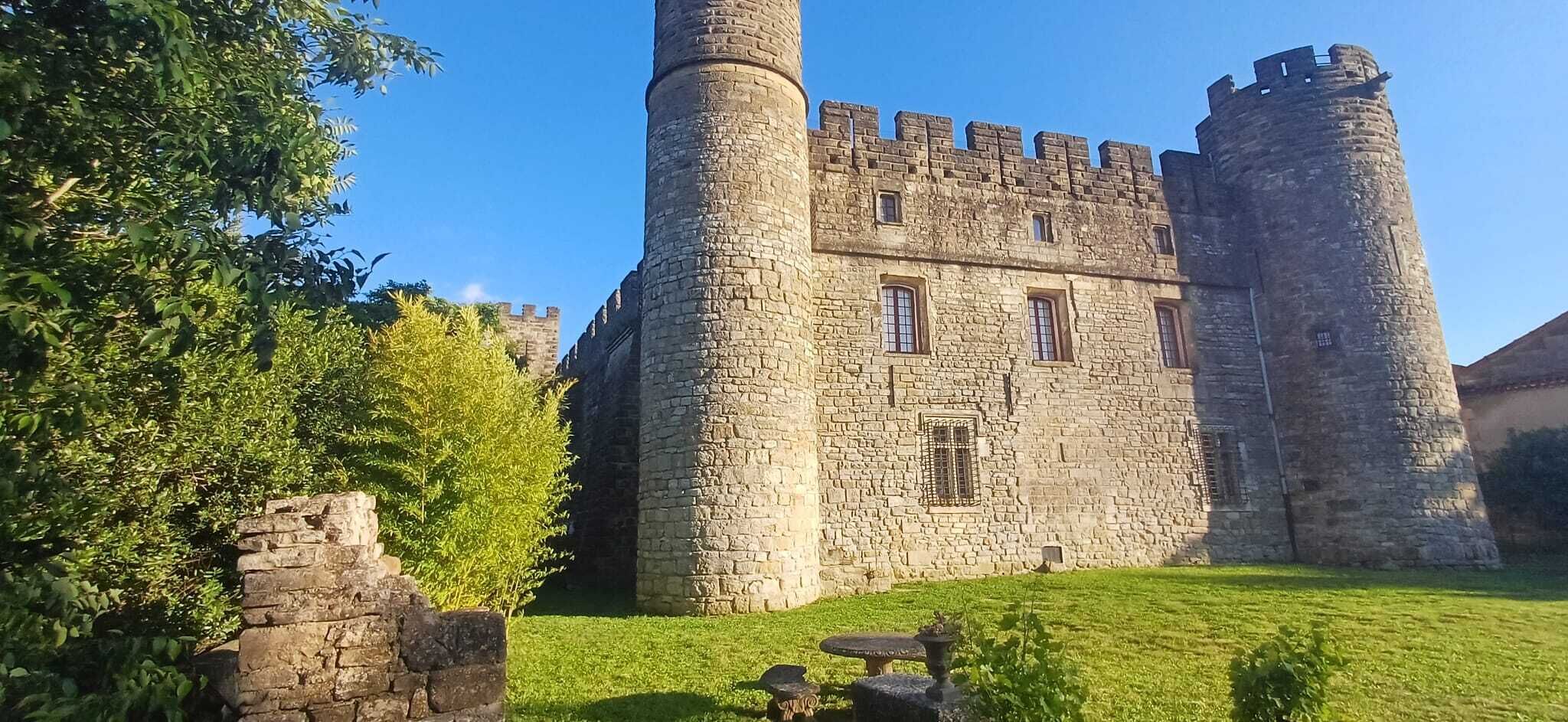 Eine historische Burg aus Stein mit zwei markanten Türmen, einem zentralen Eingang und einem gepflegten Rasen.