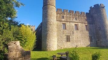 Eine historische Burg aus Stein mit zwei markanten Türmen, einem zentralen Eingang und einem gepflegten Rasen.