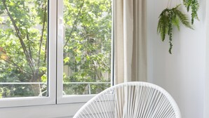 Ein Zimmer mit einem weißen Korbstuhl in der Nähe eines Fensters mit Blick auf Bäume.