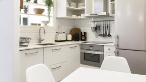 Eine moderne Küche mit weißen Schränken, einem Edelstahl-Kühlschrank, einem eingebauten Backofen und einer Kaffeemaschine.