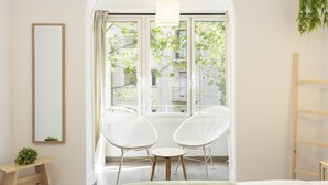 Ein Schlafzimmer mit einem großen Fenster, zwei weißen Korbstühlen, einem Nachttisch und einem Bett.