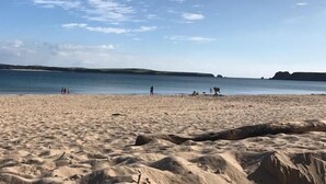 En sandstrand med ett lugnt hav och kullar i fjärran.