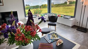 En moderne stue med et stort vindue, en sort læderstol, en vase med blomster og et magasin på bordet.