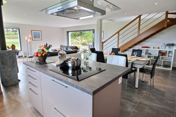 A modern kitchen with a central island, dining area, and a staircase leading to an upper level.