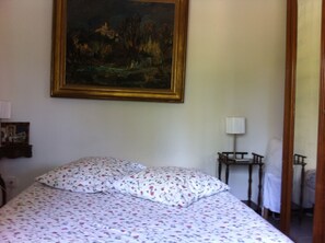A bedroom with a bed, a painting on the wall, a bedside table with a lamp, and a mirror. - Cabanon provençale (La Seyne-Sur-Mer)