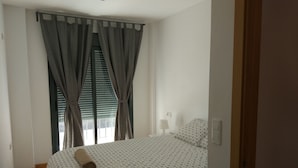 Une chambre à coucher avec un lit, des rideaux, une lampe de chevet et une fenêtre avec des stores.