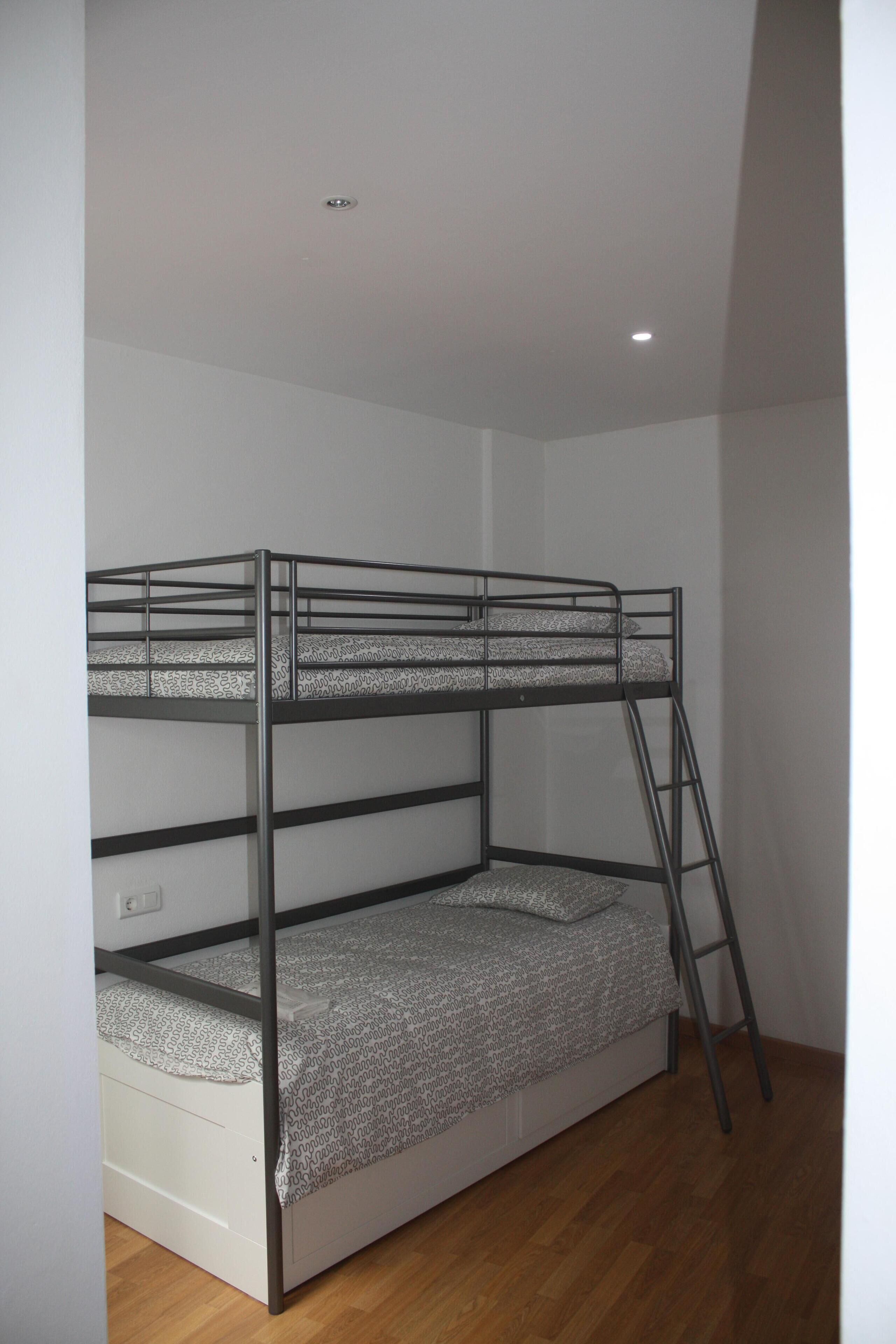 A bunk bed with a ladder, white walls, and wooden flooring.