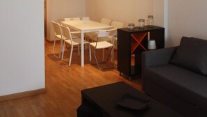 Un salon moderne avec un canapé foncé, une table basse et un coin repas comprenant une table et des chaises blanches.