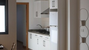 Une cuisine moderne avec des armoires blanches, un four encastré et une hotte de cuisine en acier inoxydable. On y trouve également un coin repas avec une table noire et une chaise.