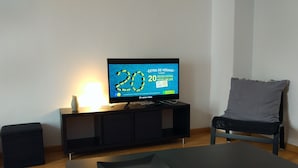 Un salon moderne avec un téléviseur à écran plat posé sur un meuble noir, un canapé noir et une table basse noire sur laquelle se trouve un plateau bleu.
