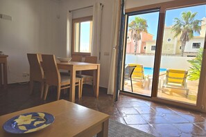 A dining area with a table and chairs, a window, and a view of a pool and palm trees. - DomusIberica Burgau, 2 bedroom house with A/C, private pool, walk to the beach! (Burgau)