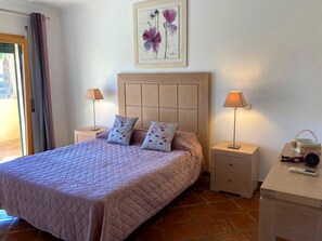 A neatly arranged bedroom with a large bed, two bedside tables, a nightstand, a lamp, and a small table with a handbag and a remote control. - DomusIberica Burgau, 2 bedroom house with A/C, private pool, walk to the beach! (Burgau)