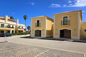 Una calle con dos edificios amarillos, una señal de parada y un coche.