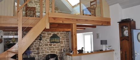 A loft-style room with a wooden staircase, stone walls, a fireplace, and a large skylight.