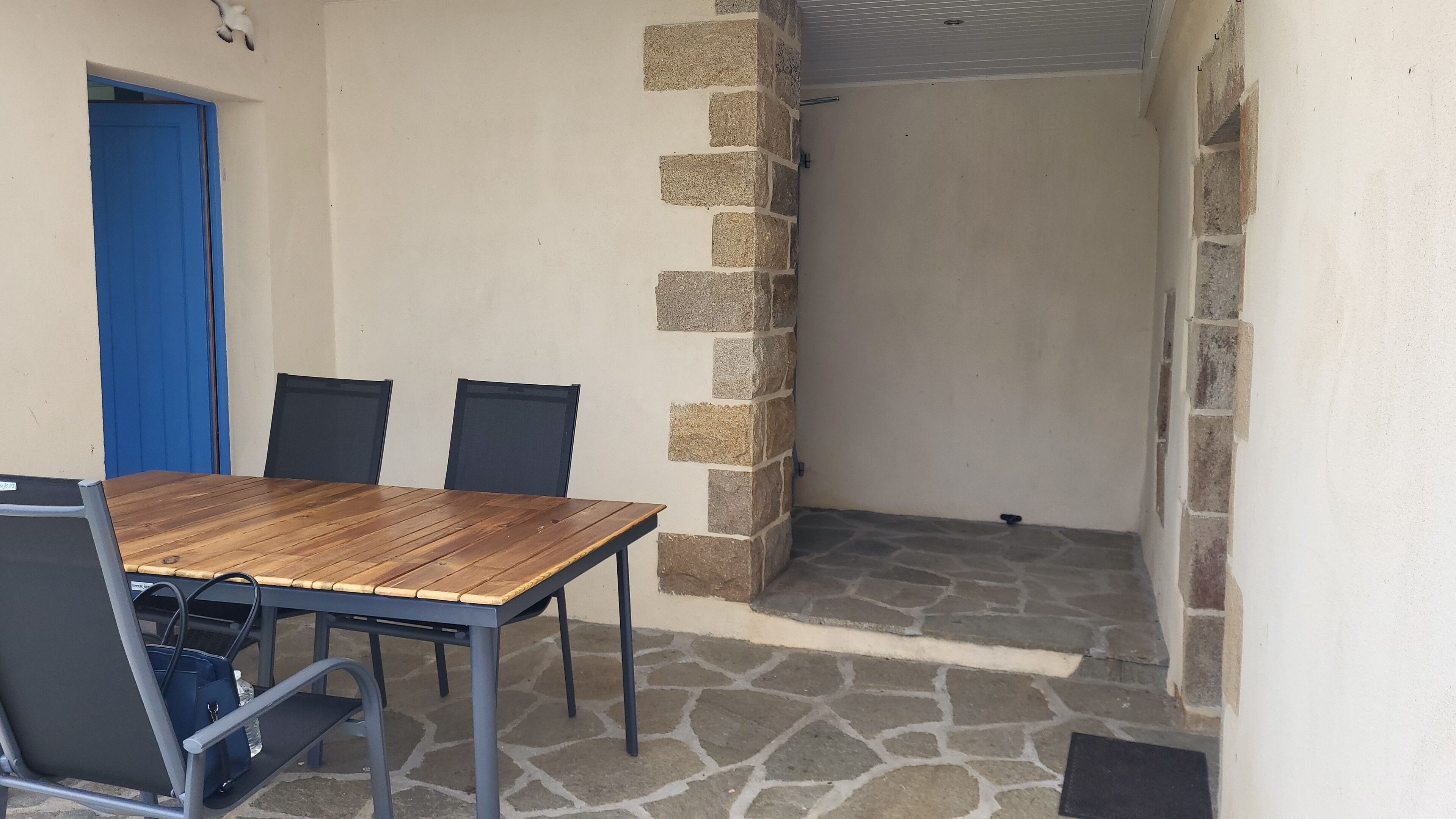A room with a wooden table and four chairs, a blue door, and a stone wall.