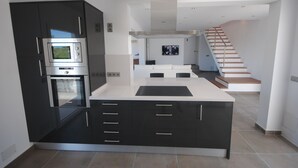 Una cocina moderna con horno empotrado, una isla grande con cajones y una escalera que lleva a una sala de estar.
