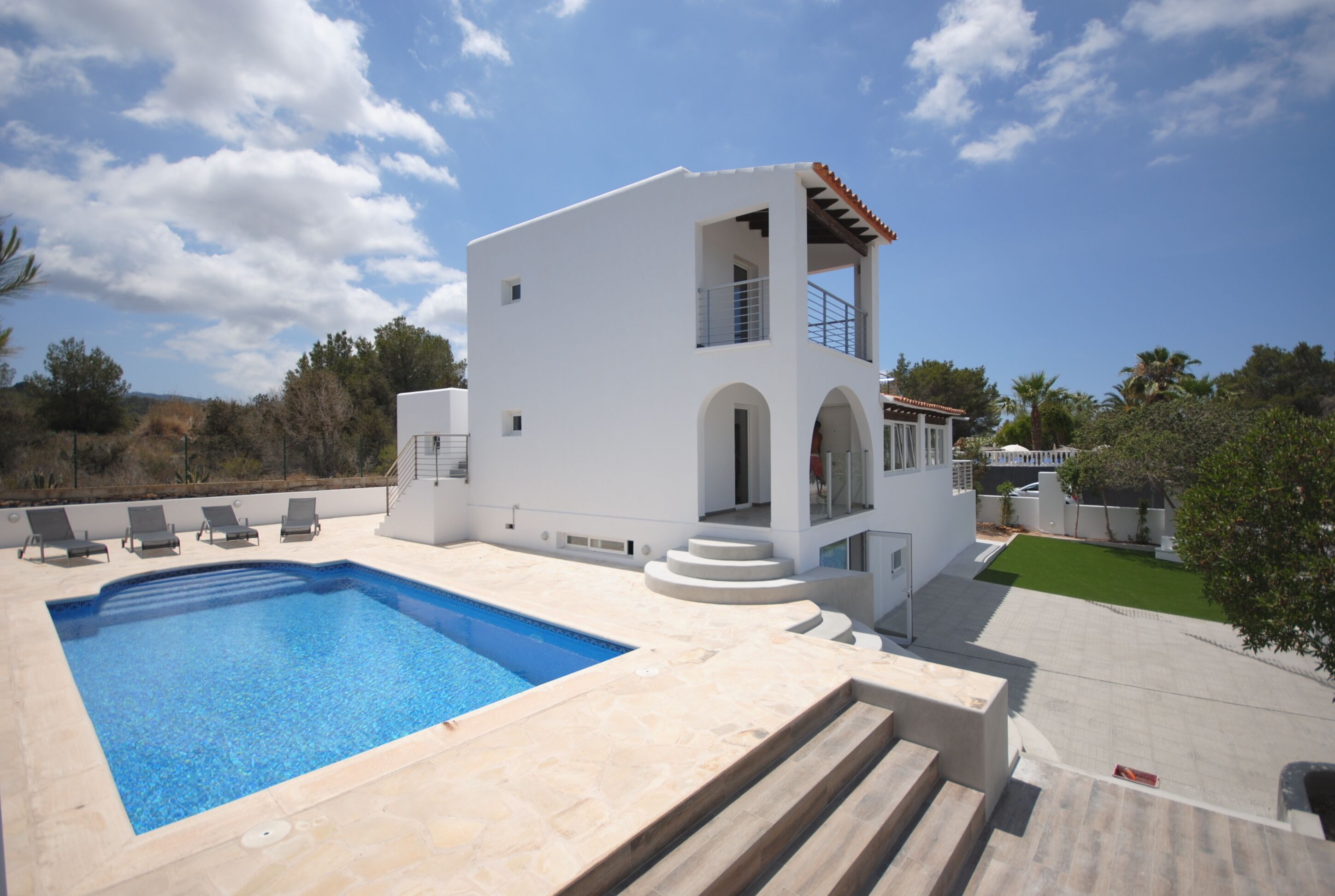 Eine moderne, weiße Villa mit Swimmingpool, Balkon und kleinem Garten.