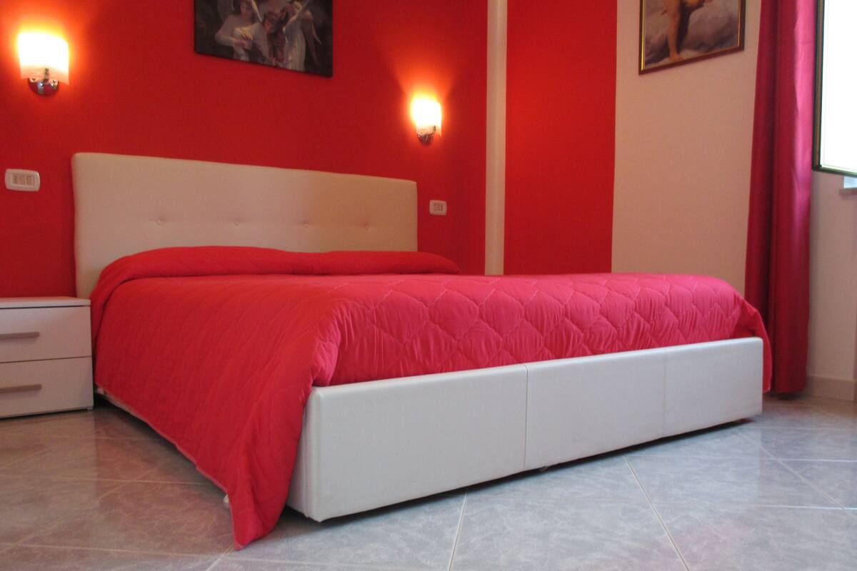 A bed with a red bedspread in a room with red walls and two wall-mounted lights.
