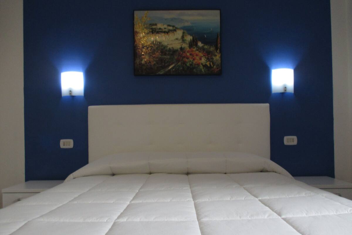 A bedroom with a large bed, two bedside lamps, and a painting on the wall.