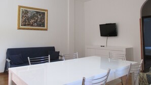 A dining area with a white table and chairs, a black TV mounted on the wall, and a framed painting above the table. - Casa Vacanze Donna Antonia (Centola)